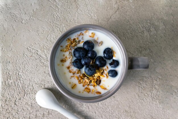 Mirtilli muesli allo yogurt in una tazza su intonaco grigio