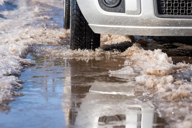 Miscela di neve e acqua sulla strada nella soleggiata giornata primaverile Auto disgelo stagionale che guida strada sporca e bagnata