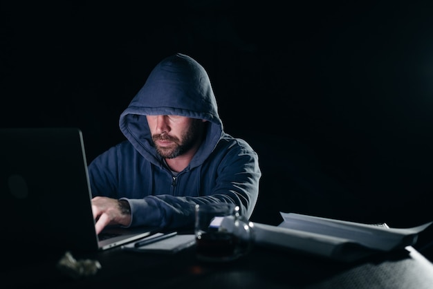 Misterioso criminale in un cappuccio hackera un laptop al buio