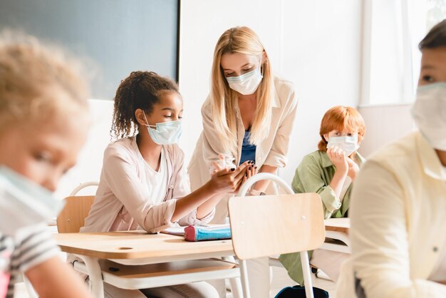 Misure sanitarie contro la diffusione del coronavirus Covid-19 a scuola L'insegnante usa il disinfettante con i suoi studenti Gli studenti indossano maschere protettive prima della lezione