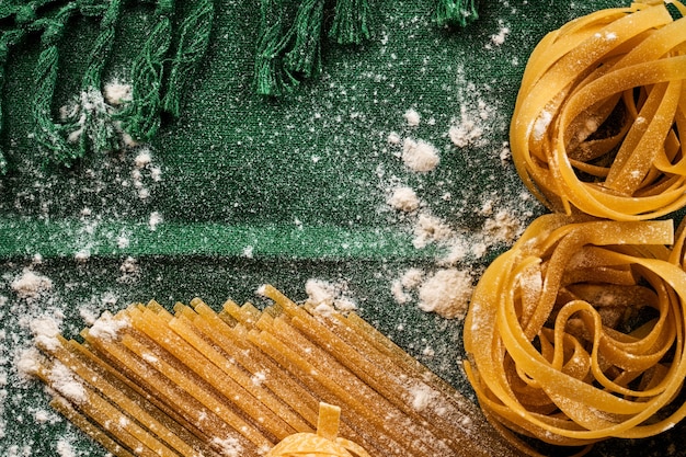 Mix di diverse varietà di pasta su sfondo di tessuto verde, cucinando maccheroni assortiti concept