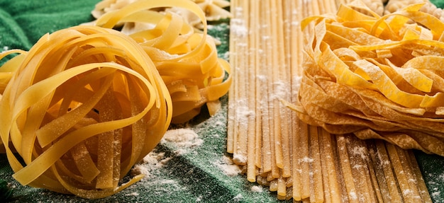 Mix di diverse varietà di pasta su sfondo verde tessuto, cucinare maccheroni assortiti concetto