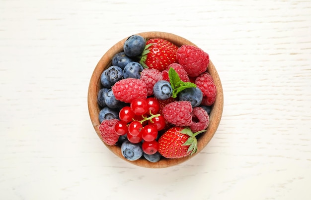 Mix di diversi frutti di bosco freschi in una ciotola sulla vista del tavolo in legno bianco