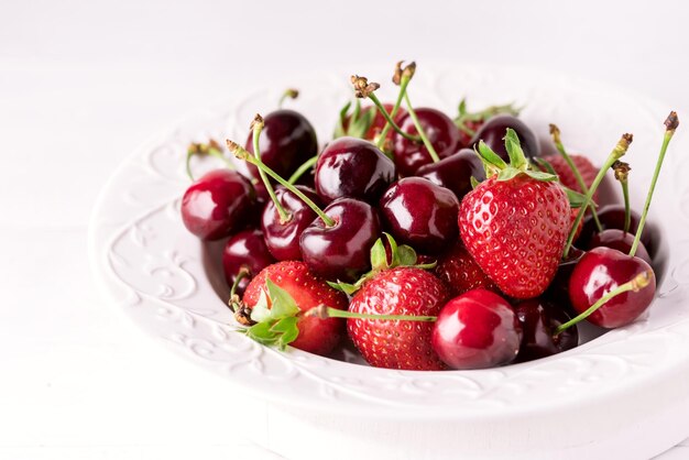 Mix di fragole e ciliegie in piatto bianco Bella fragola succosa matura e ciliegia Close Up