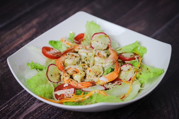 Mix di insalata con gamberetti nel piatto bianco sul tavolo in legno, ravanello e pomodorini, cibo sano.
