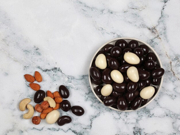 Mix di noci ricoperte di cioccolato e crudo su sfondo di marmo grigio. Vista dall'alto con copia spazio