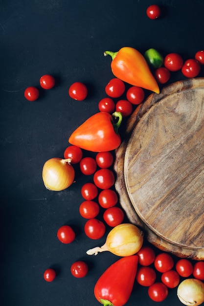 Mix di pomodorini freschi crudi pepe cipolla ed erbe aromatiche su tavola di pietra scura e tavola di legno vuota