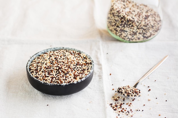 Mix di quinoa bianca rossa e nera cruda in una ciotola e in un cucchiaio su un panno Cibo sano senza glutine