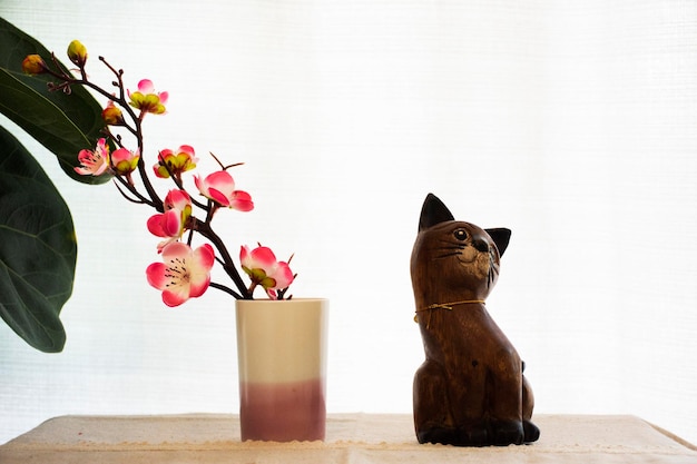 Mobili per la decorazione d'interni e gatto dei cartoni animati in legno con vaso in ceramica e ramo di fiori di sakura su sfondo tenda bianca nel soggiorno della casa per i thailandesi riposati rilassati a Nonthaburi Thailandia