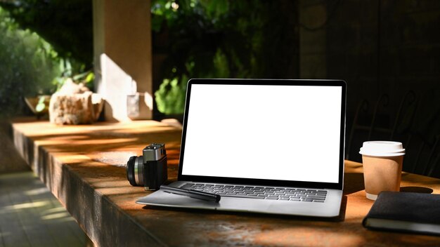 Mock up computer portatile con tazza di caffè a schermo vuoto e fotocamera su un tavolo di legno