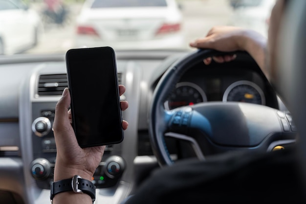 Mock up di un uomo che utilizza uno smartphone mobile all'interno di un'auto Conducente che tiene la mano con uno smartphone a schermo nero vuoto che cerca l'indirizzo e la posizione del pin tramite l'applicazione di navigazione della mappa tecnologia dei trasporti