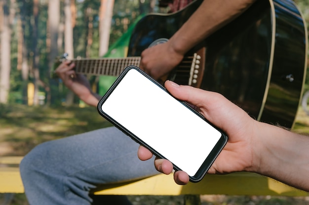 Mock up di uno smartphone davanti a un uomo che suona la chitarra. Sullo sfondo della foresta.