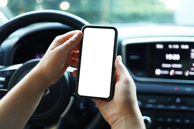 Mock up immagine, ragazza che utilizza uno smartphone mobile con schermo bianco vuoto all'interno di un'auto in una giornata di sole, toccando lo schermo o inviando messaggi di testo, copia spazio per la tua pubblicità