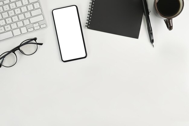 Mock up smart phone notebook tazza di caffè e bicchieri sulla scrivania dell'ufficio bianco