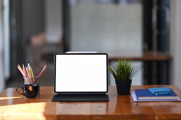 Mock up tablet con tastiera wireless, cancelleria e notebook sulla scrivania in legno.