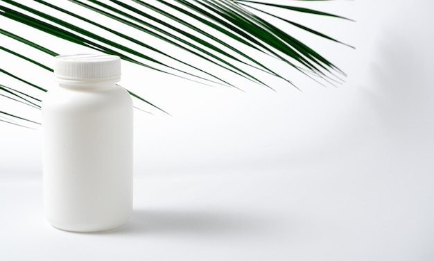 Mockup Bottiglia di plastica bianca per vitamine cosmetici prodotti per la cura della salute su uno sfondo bianco con foglie di palma verdi Prodotto cosmetico medico di bellezza