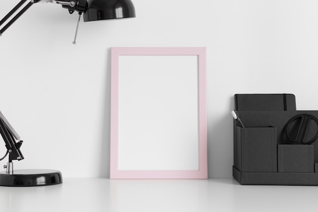 Mockup con cornice rosa con una lampada e accessori per l'area di lavoro su un tavolo bianco Orientamento verticale