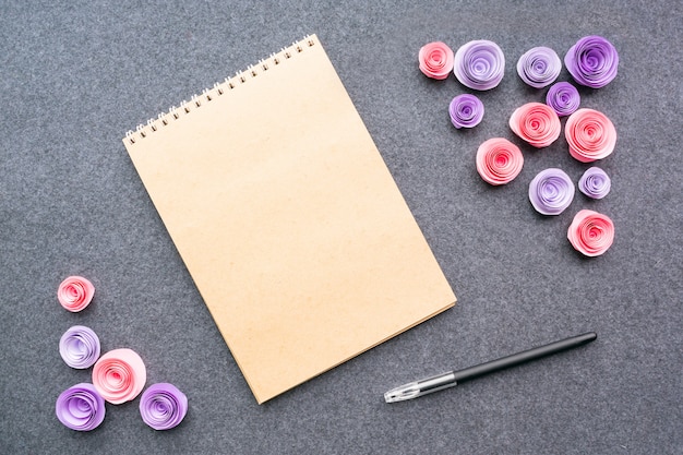 Mockup con la penna vuota del taccuino e le rose rosa di carta