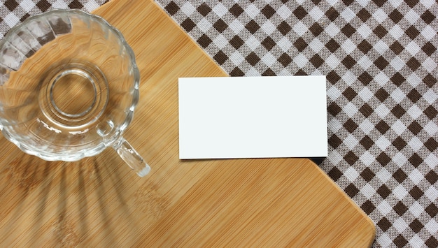 Mockup, creatore di scene. carta vuota, tazza di vetro e tagliere di bambù su una tovaglia a scacchi, vista dall'alto. tavolo della cucina. copia spazio.