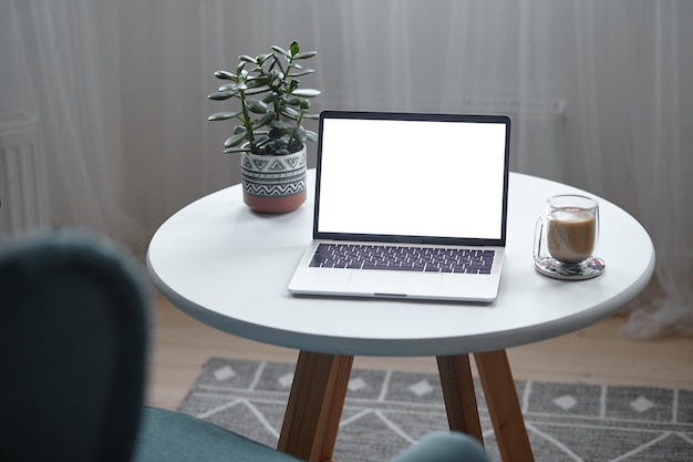 Mockup dello schermo del computer portatile sul tavolo con tazza di caffè e pianta d'appartamento a casa senza persone