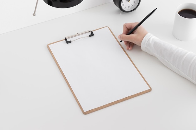 Mockup di appunti in legno con una lampada a tazza dell'orologio su un tavolo bianco e con una donna che prende appunti