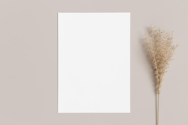 Mockup di biglietto d'invito bianco con una decorazione di erba secca su un tavolo beige 5x7