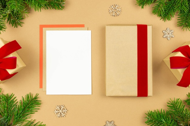 Mockup di biglietto di auguri di Natale e modello di confezione regalo avvolto con nastro rosso e decorazione di rami di albero di Natale su sfondo di carta Composizione in stile piatto laico festivo Vista dall'alto