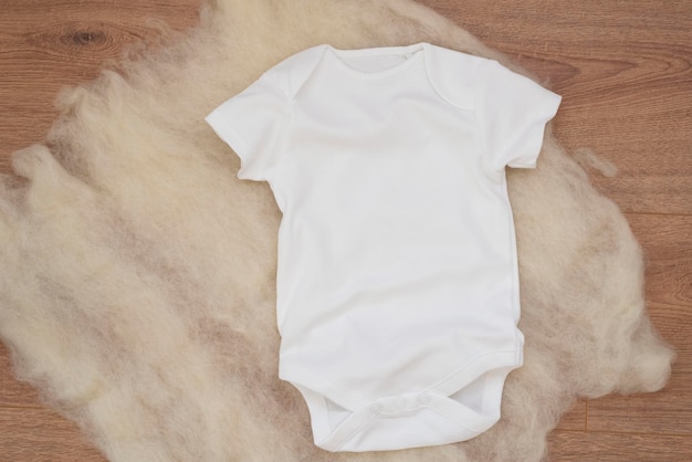 Mockup di bodysuit bianco per bambini su sfondo di legno con giocattolo colorato modello di vestiti per bambini vuoti