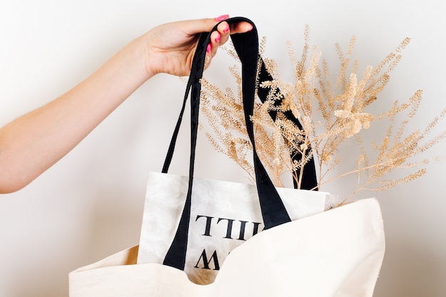 Mockup di borsa a mano femminile in ecobag riutilizzabile in cotone bianco con manici neri con fiori secchi e ...