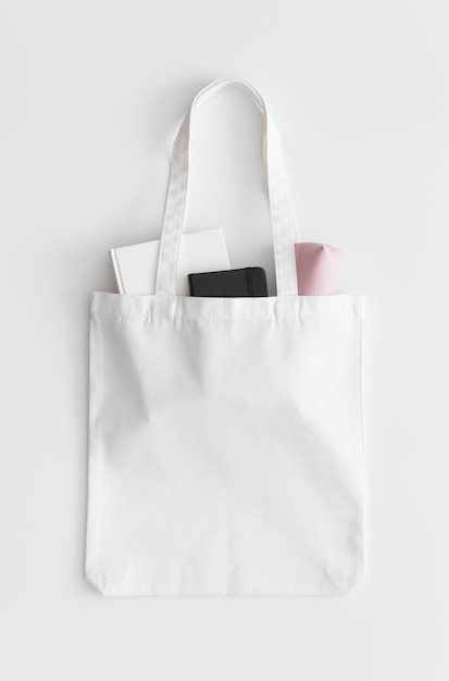 Mockup di borsa tote bianca con un quaderno e una custodia su un tavolo bianco