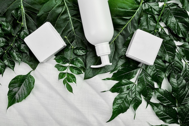 Mockup di bottiglia bianca vuota su foglie tropicali verdi, packaging cosmetico, vista dall'alto del tubo crema, composizione piatta