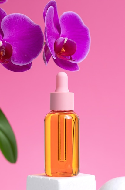 Mockup di bottiglia di vetro su sfondo rosa I fiori di orchidea rosa si trovano accanto alla bolla con olio Concetto di trattamenti termali per la cura della pelle cosmetici naturali