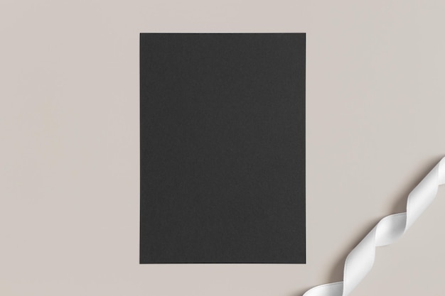 Mockup di carta nera dell'invito con un nastro di raso su un rapporto 5x7 di sfondo beige simile a A6 A5