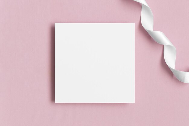 Mockup di carta quadrata dell'invito con un nastro di raso su un tessuto rosa tenue