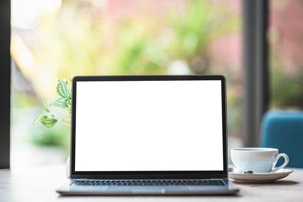 Mockup di computer portatile con schermo vuoto con tazza di caffè e smartphone sul tavolo dello sfondo della caffetteria, schermo bianco