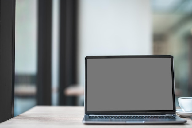 Mockup di computer portatile con schermo vuoto con tazza di caffè e smartphone sul tavolo dello sfondo della caffetteria, schermo grigio nero