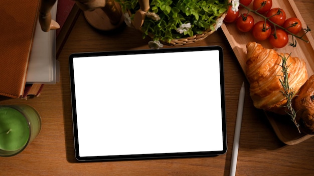 Mockup di computer tablet con colazione sul tavolo di lavoro concetto croissant pomodori su piatto di legno