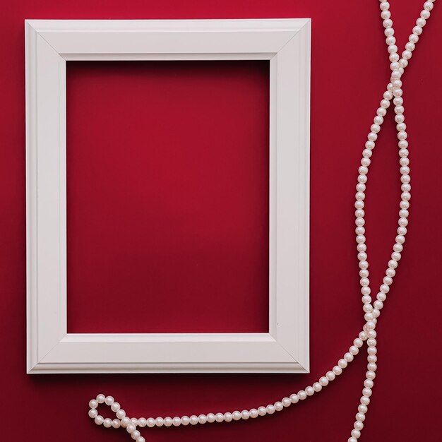 Mockup di cornice artistica verticale bianca e gioielli di perle su sfondo rosso come concetto di stampa di opere d'arte di design flatlay o album fotografico