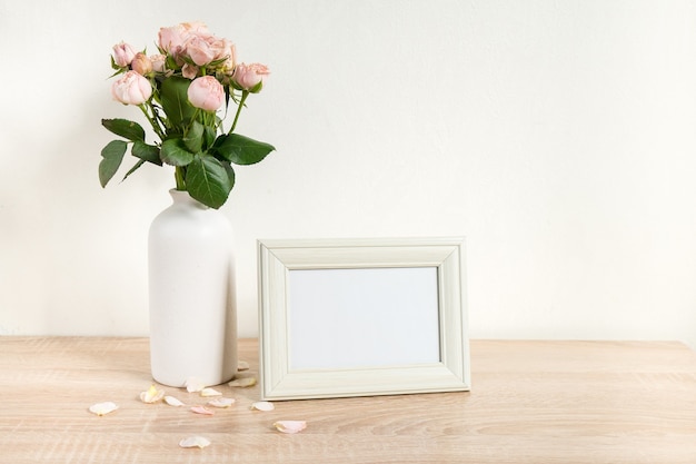 Mockup di cornice immagine bianco ritratto su tavola di legno Vaso moderno in ceramica con rose Sfondo muro bianco Interni scandinavi