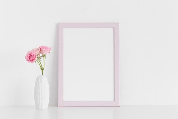 Mockup di cornice rosa con rose rosa in un vaso su un tavolo biancoOrientamento verticale