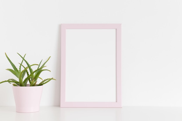 Mockup di cornice rosa con una pianta succulenta in una pentola su un tavolo bianco Orientamento verticale