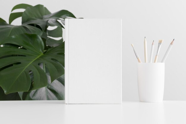 Mockup di libro bianco con accessori per l'area di lavoro e una pianta monstera