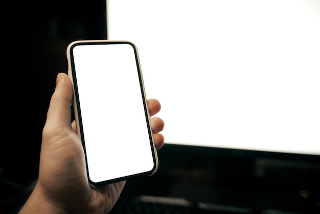 Mockup di mano che tiene uno smartphone moderno con monitor per PC sullo sfondo Schermata vuota