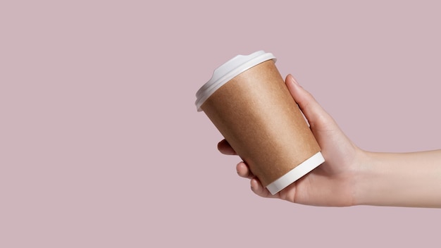 Mockup di mano di donna che regge una tazza di carta da caffè su sfondo rosa