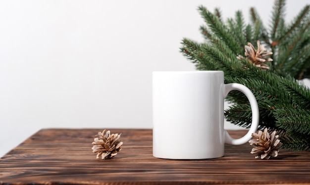 Mockup di Natale una tazza da tè bianca vuota su un tavolo di legno marrone e rami di una corona di albero di Natale. Modello di tazza per il tuo design, logo con spazio di copia. Capodanno