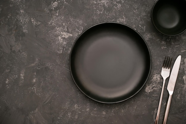 Mockup di piatto in ceramica nera con ciotola di salsa nera e posate su sfondo scuro