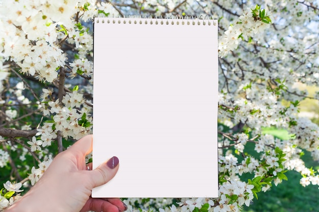 Mockup di primavera estate con quaderno bianco in mano femminile