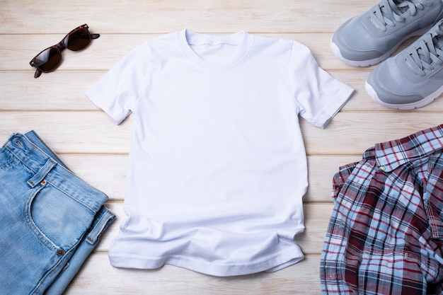 Mockup di t-shirt in cotone da uomo bianco con occhiali da sole, scarpe da corsa grigie, jeans blu e camicia a scacchi. Modello di maglietta di design, presentazione di stampa t-shirt mock up