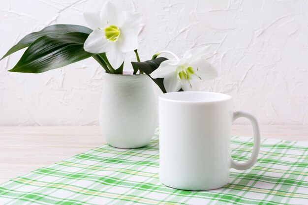 Mockup di tazza bianca con giglio in vaso sul tovagliolo a scacchi verde