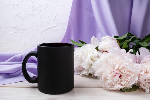 Mockup di tazza da caffè nero con peonia rosa pallido e sciarpa lilla. Tazza vuota mock up per la promozione del marchio